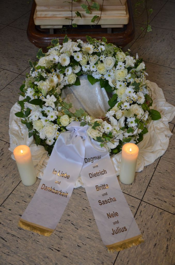 Stilvolle Trauerdekoration mit weißem Kranz, Kerzen und Sarg in der Gerricus-Kapelle - Bestatter Düsseldorf, Bestattung Düsseldorf.