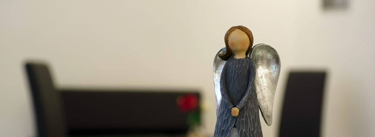 Eine stilvolle Engelsfigur steht im Fokus vor einer dezent eingerichteten Trauerhalle bei Ihrem Bestatter Düsseldorf - Bestattung Düsseldorf.