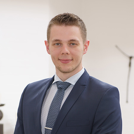 Junger Bestatter im Anzug bei Vogt & Kamp Bestattungen Düsseldorf, freundlich vor hellem Hintergrund. Bestattung Düsseldorf.