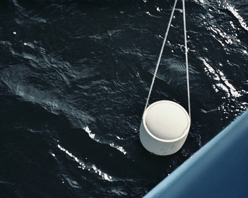 Eine weiße Boje schwebt an Seilen über dunklem Wasser am blauen Boot - Symbolbild für Bestatter Düsseldorf, Bestattung Düsseldorf.