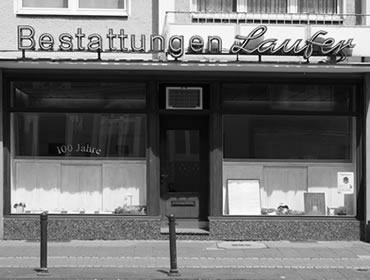 Schwarzweißfoto eines Bestattungshauses in Düsseldorf mit der Aufschrift "Bestattungen Laufer", Schaufenster mit "100 Jahre".