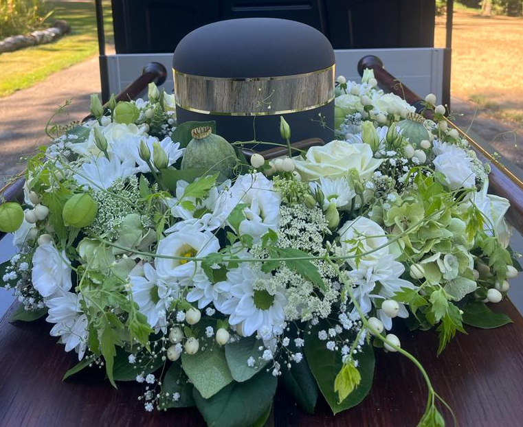 Stilvolle schwarze Urne mit Silberband im Blumengesteck - würdevolle Bestattung in Düsseldorf durch Ihren Bestatter Vogt & Kamp.